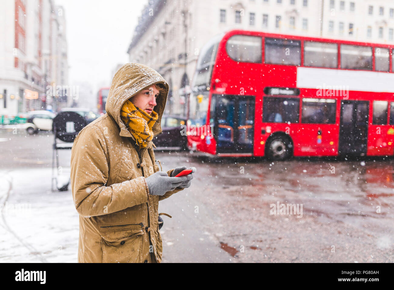 UK, Londra, giovane con un telefono cellulare in piedi alla strada guardando a distanza Foto Stock