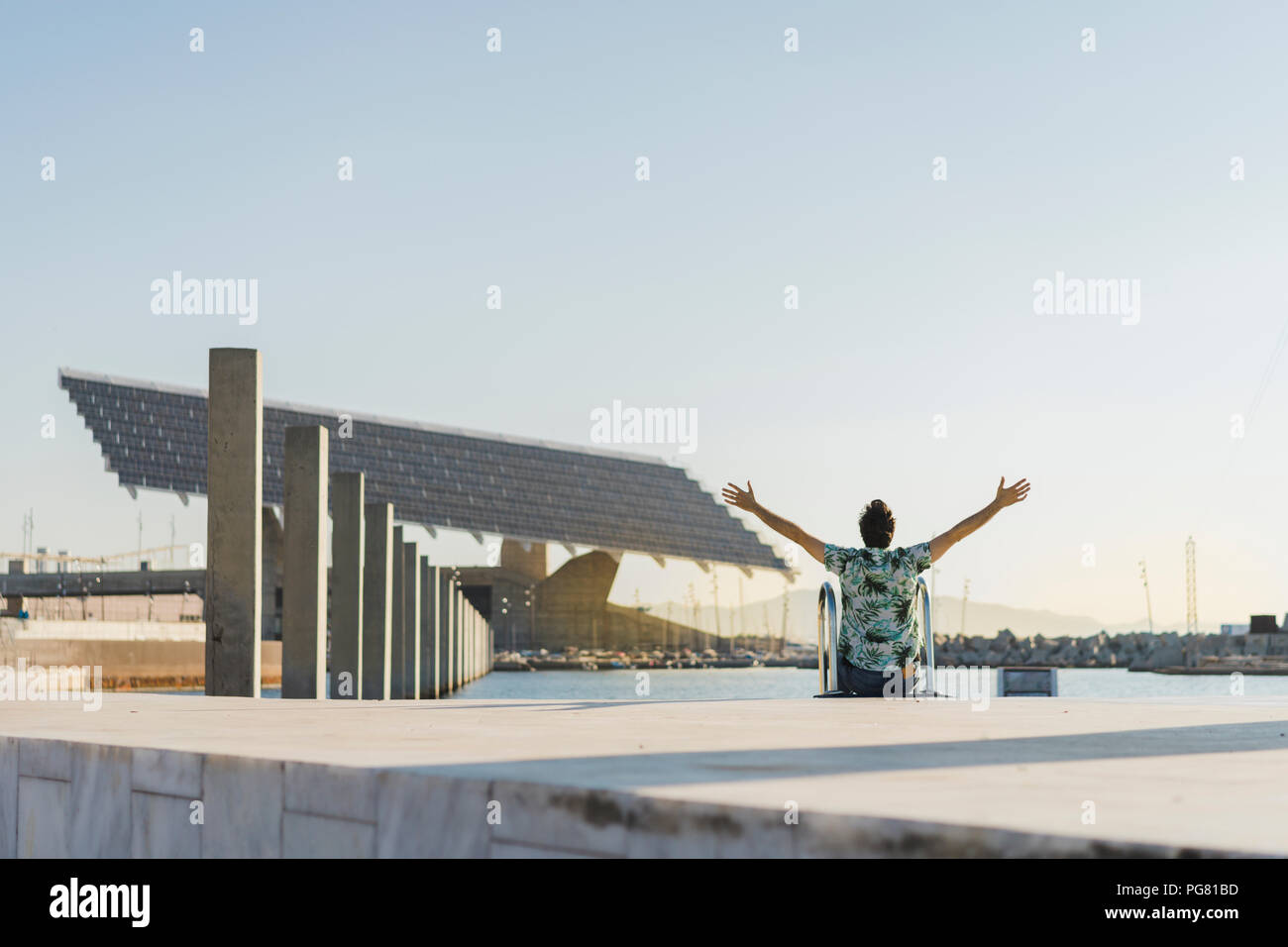 Uomo seduto in piscina il bordo con le braccia in alto per godersi la vita, vista posteriore Foto Stock