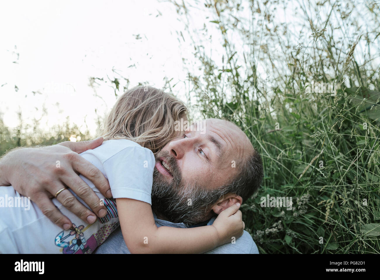 Padre e figlia piccola giacente insieme su un prato che abbraccia ogni altro Foto Stock