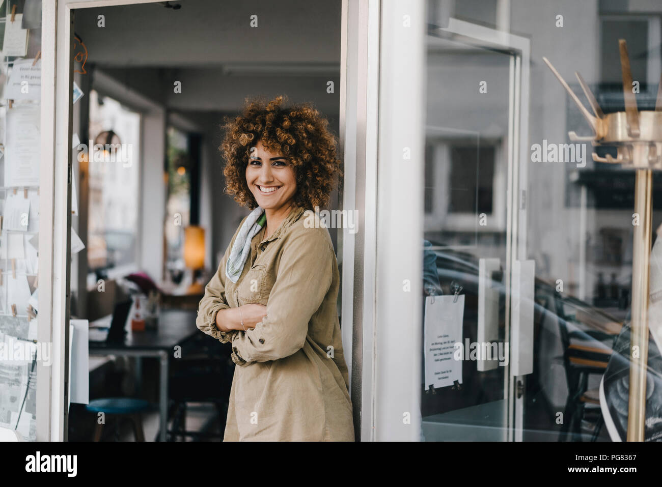 Donna sorridente in piedi con le braccia incrociate nella porta di coworking space Foto Stock