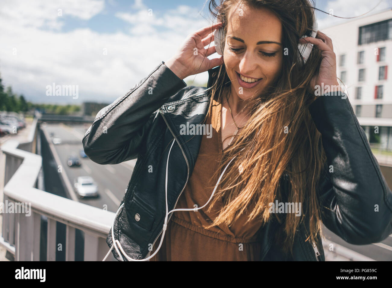 Sorridente giovane donna ascolto di musica sul ponte autostradale Foto Stock
