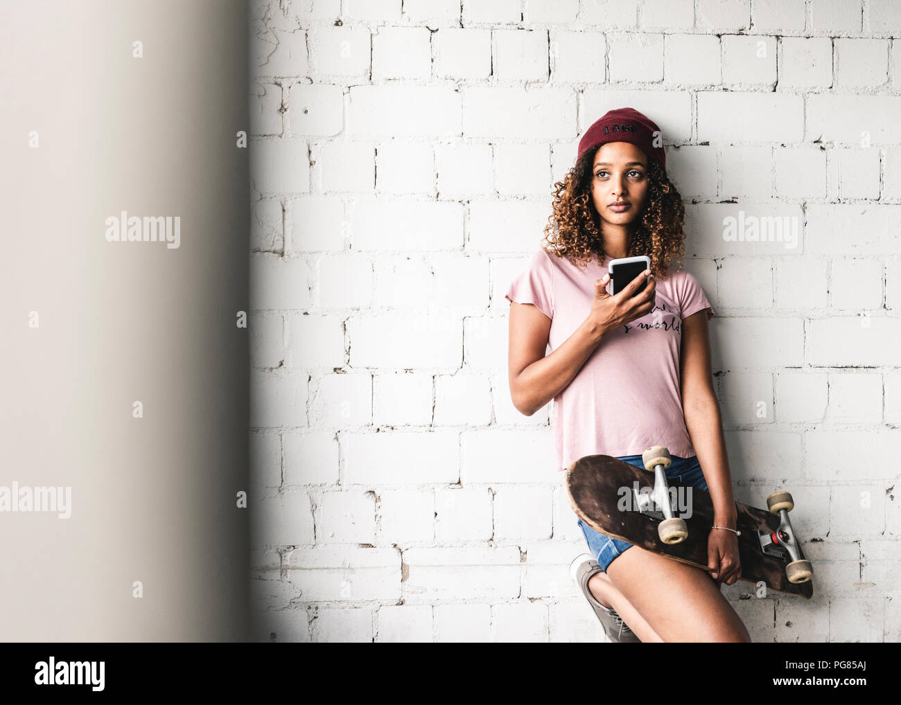 Ritratto di una giovane donna con lo skateboard, appoggiata contro la parete Foto Stock