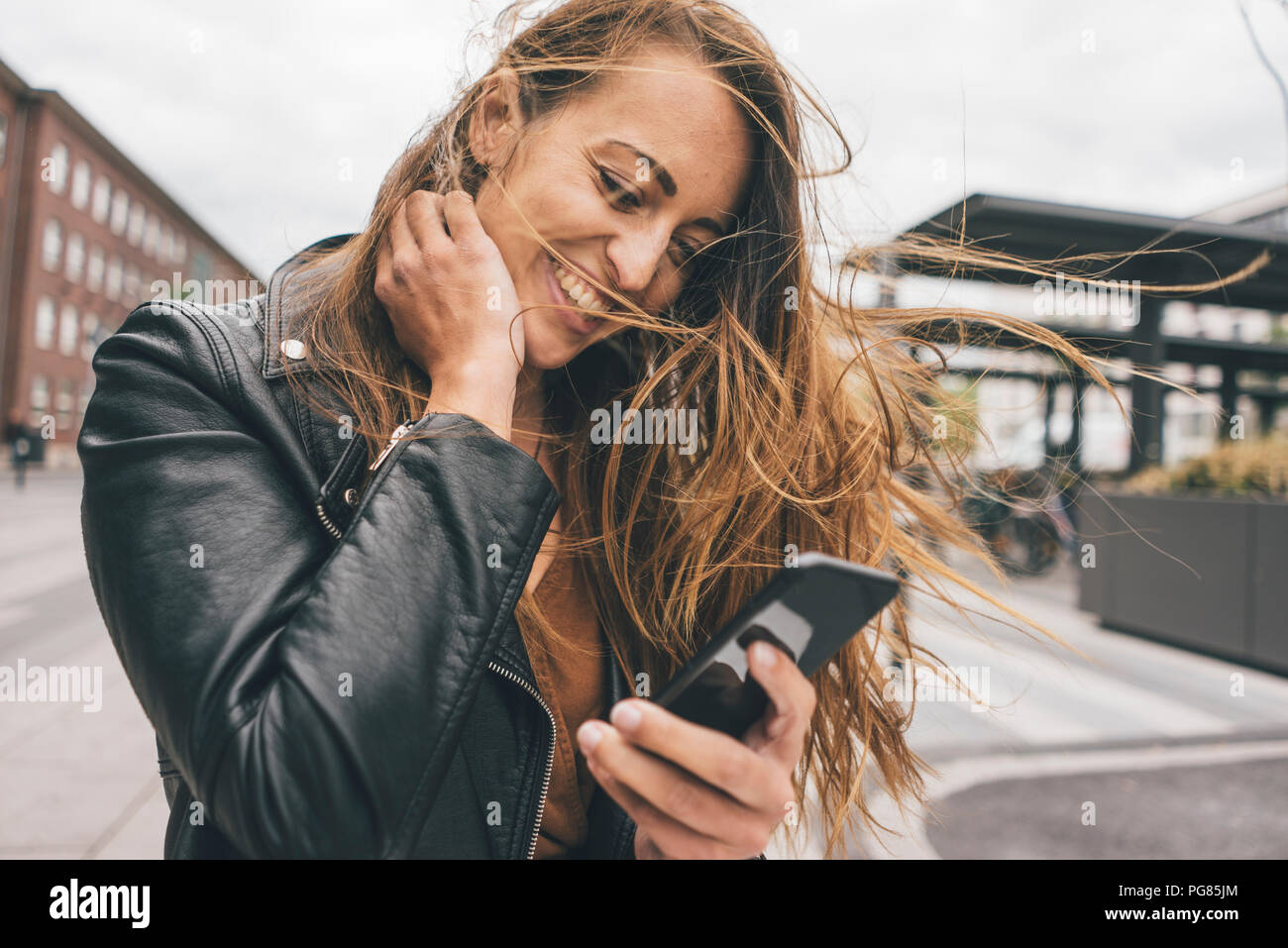 Felice giovane donna con capelli spazzate dal vento utilizzando il cellulare in città Foto Stock