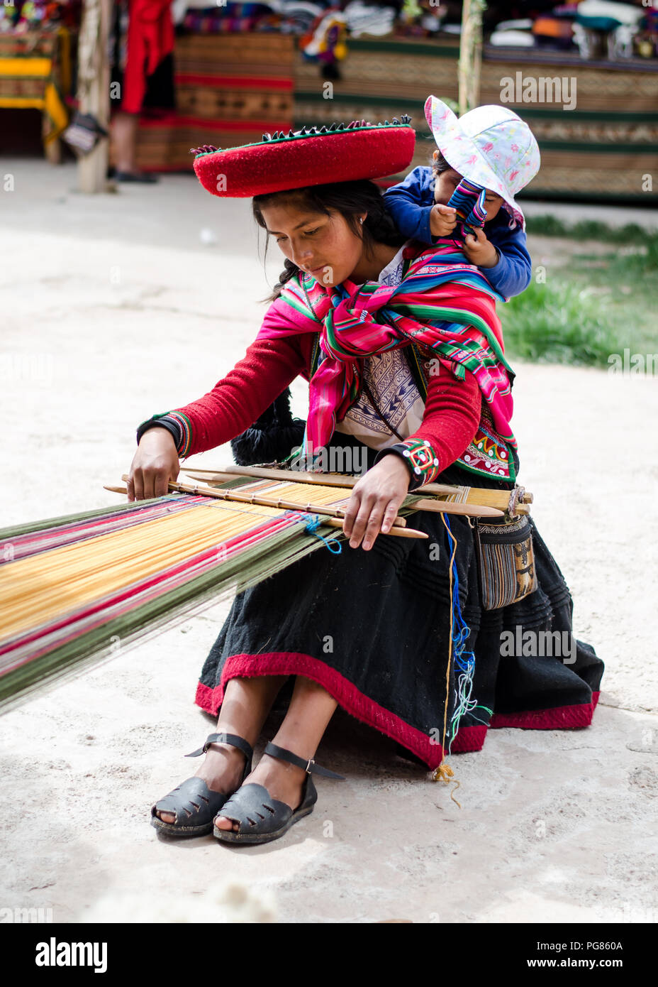 Il quechua donna tessitura di tessuti e portando il suo bambino Foto Stock