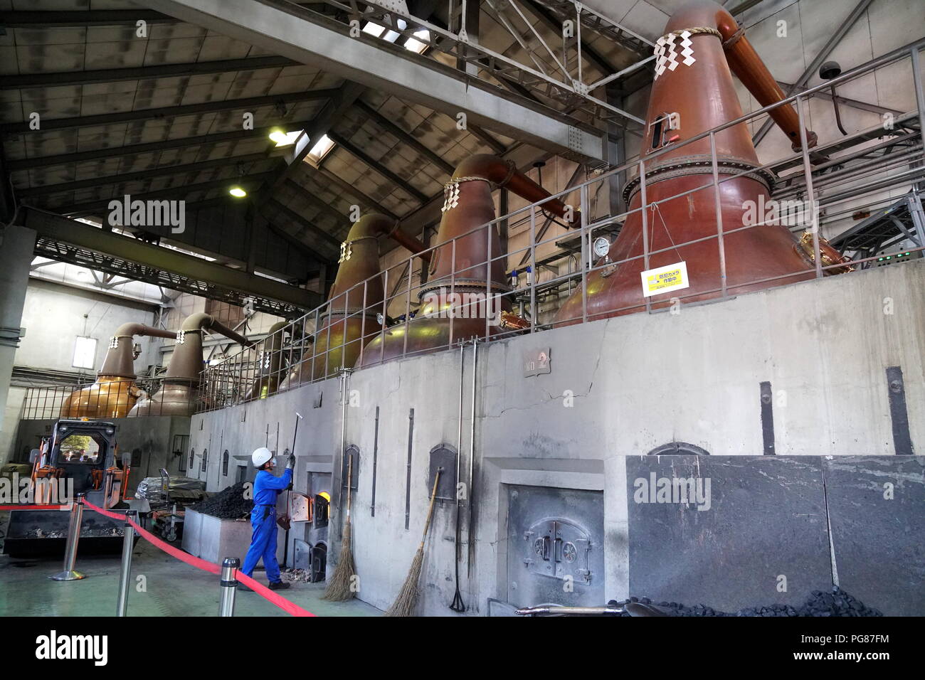 Hokkaido Asahi la Fabbrica di Birra di Sapporo, Hokkaido, Giappone. Un lavoratore di mettere il carbone nel forno con le impressionanti immagini fisse che incombe sopra. Foto Stock