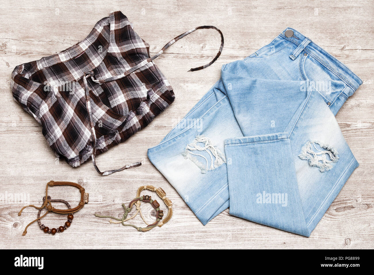 Hippie stile di moda donna vestito. Controllare cotone camicia, jeans strappati, corda legno braccialetti del tallone sul malandato sfondo di legno Foto Stock