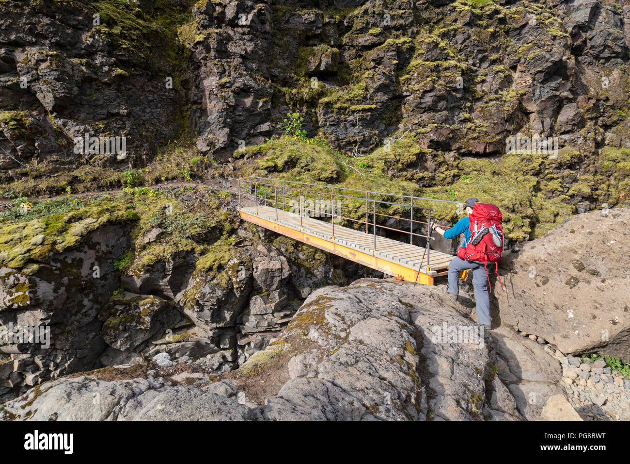 Una femmina solitario escursionista attraversando un ponte sul Laugavegur trail in Islanda. Foto Stock