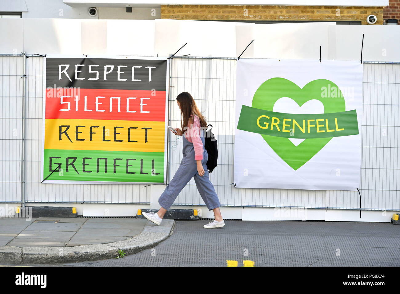 Una donna cammina passato banner a Grenfell torre in Notting Hill, West London, precedendo il carnevale di Notting Hill. Foto Stock