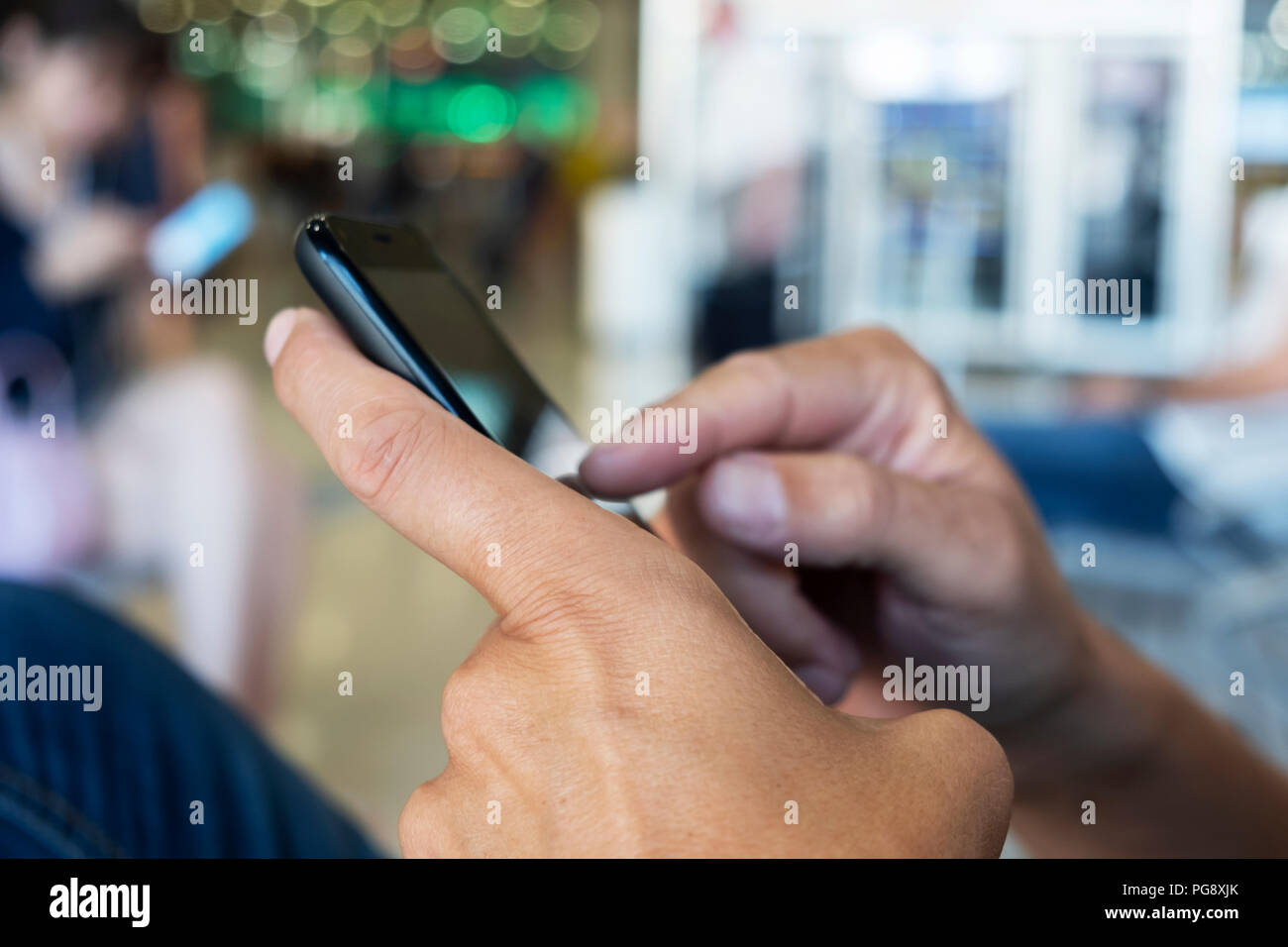 Primo piano di un giovane uomo caucasico utilizzando uno smartphone presso la sala di attesa di un treno o un autobus stazione, o un aeroporto Foto Stock
