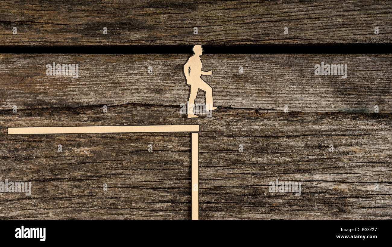 Carta ritagliata silhouette uomo di raggiungere il punto di non ritorno circa al passo fuori dal bordo di un precipizio nell evitare su legno rustico con copia spazio. Foto Stock