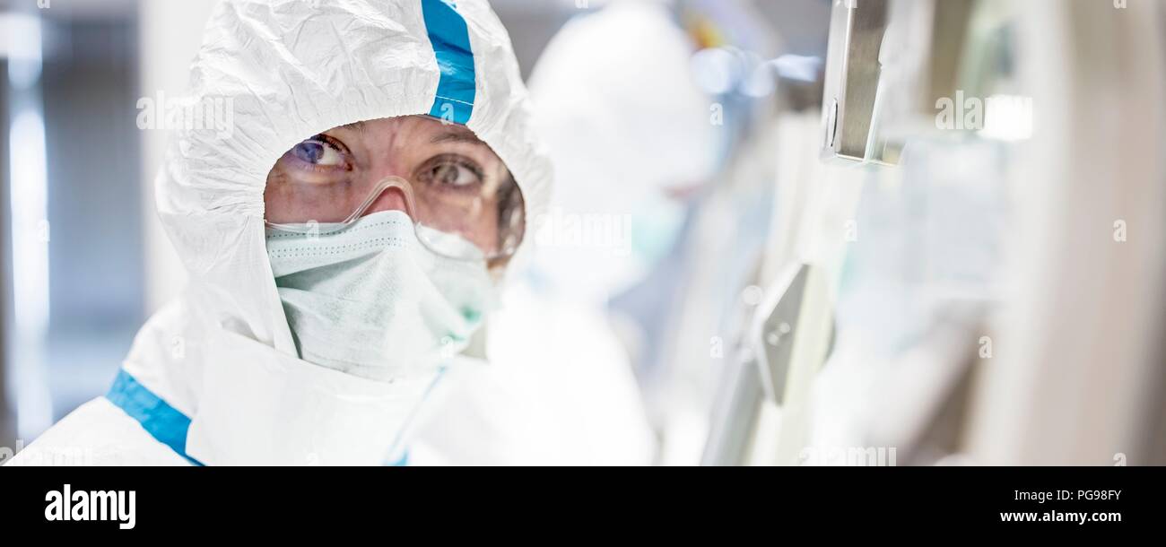 Tecnico di laboratorio che indossa una tuta protettiva, maschera viso e occhiali di sicurezza in un laboratorio che deve mantenere un ambiente sterile. Foto Stock
