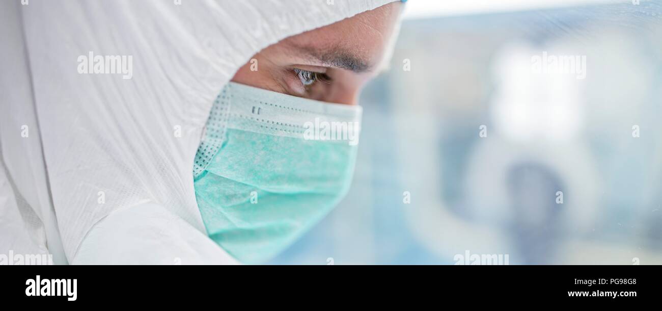 Close-up di un tecnico di laboratorio che indossa una tuta protettiva e maschera per il viso in un laboratorio che deve mantenere un ambiente sterile. Foto Stock