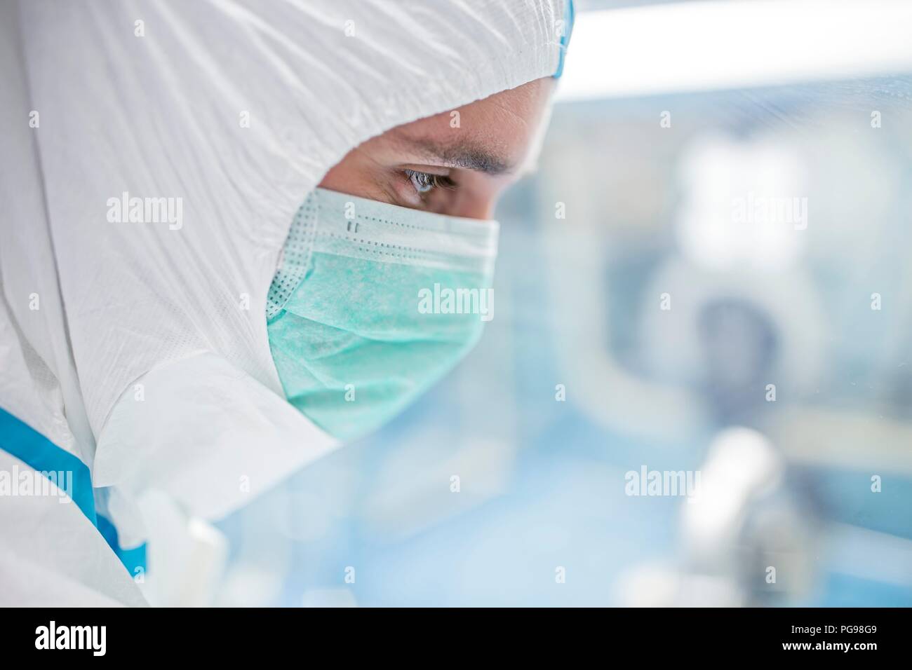 Close-up di un tecnico di laboratorio che indossa una tuta protettiva e maschera per il viso in un laboratorio che deve mantenere un ambiente sterile. Foto Stock