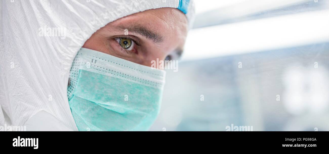 Close-up di un tecnico di laboratorio che indossa una tuta protettiva e maschera per il viso in un laboratorio che deve mantenere un ambiente sterile. Foto Stock