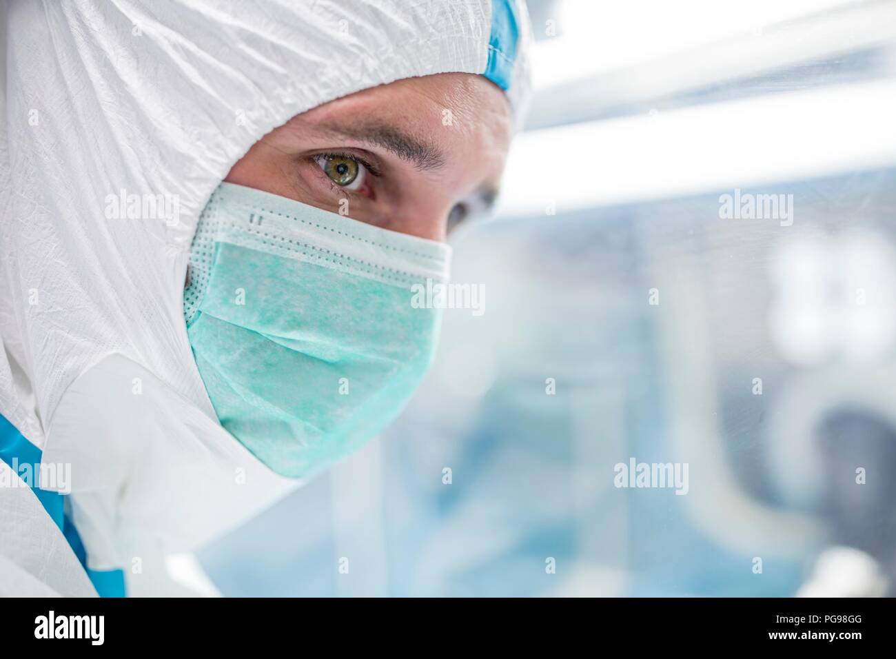 Close-up di un tecnico di laboratorio che indossa una tuta protettiva e maschera per il viso in un laboratorio che deve mantenere un ambiente sterile. Foto Stock