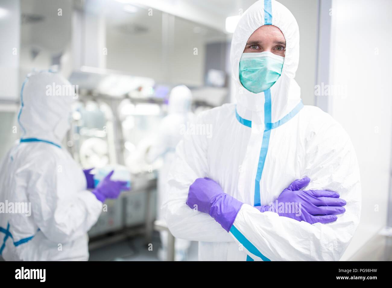 Tecnico di laboratorio che indossa una tuta protettiva e maschera per il viso in un laboratorio che deve mantenere un ambiente sterile. Foto Stock