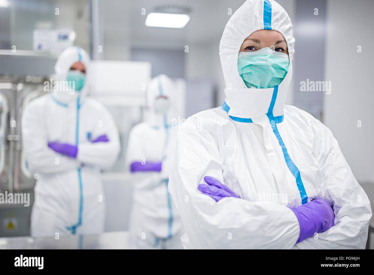 Tecnici di laboratorio indossando tute protettive e maschere facciali in un laboratorio che deve mantenere un ambiente sterile. Foto Stock
