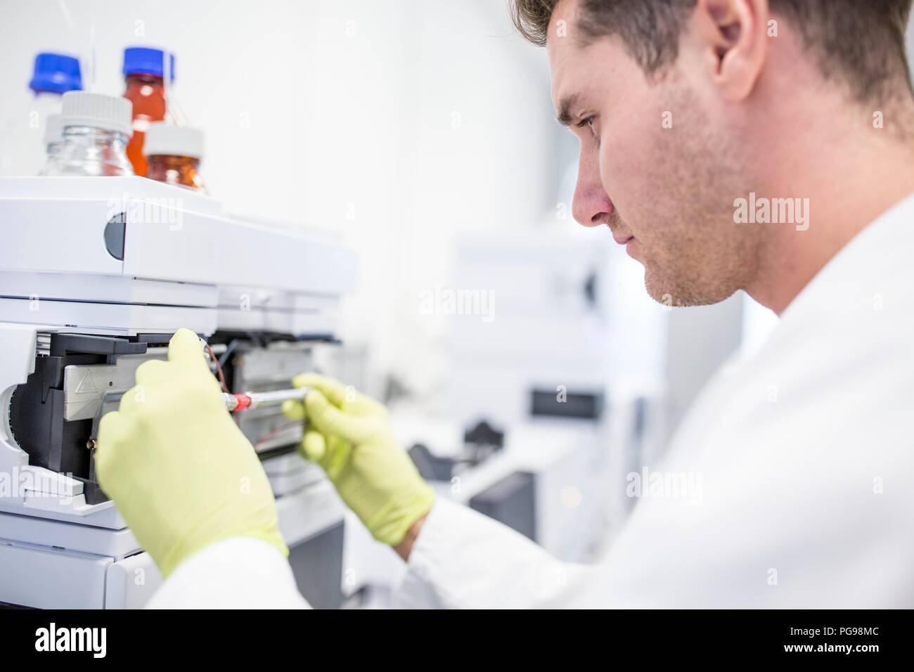 Il tecnico ponendo una colonna di vetro contenente una soluzione di calibrazione in uno spettrometro di massa. La spettrometria di massa utilizza forti campi magnetici ed elettrici per separare i componenti di un campione in massa e carica. Ciò consente ai ricercatori di determinare la composizione elementare del campione. Foto Stock