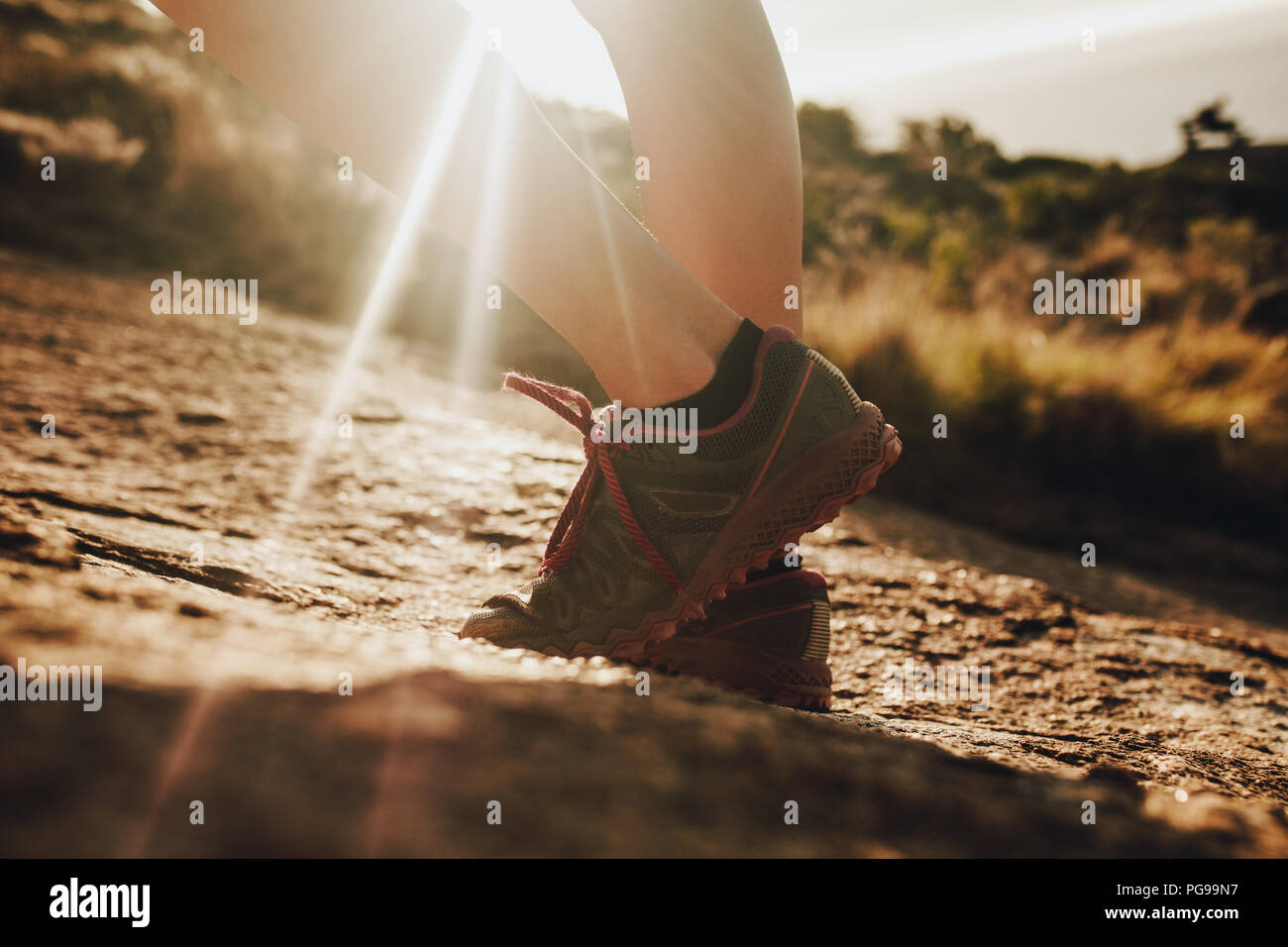 Close up femmina sentiero di montagna runner indossa calzatura sportiva in piedi nella luce del sole. Donna in scarpe da corsa in piedi nel sentiero roccioso. Foto Stock