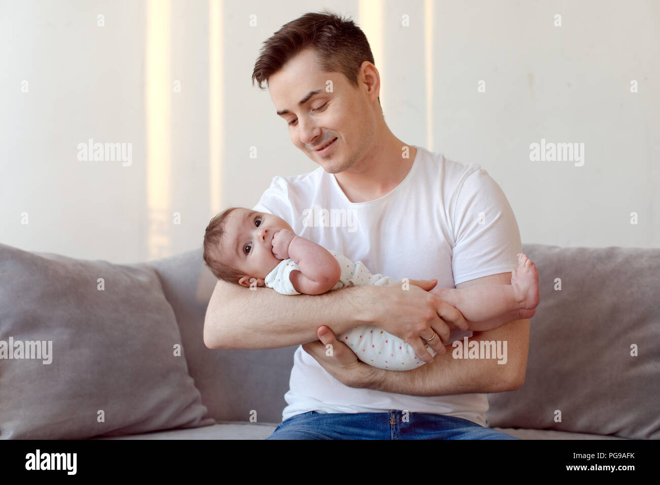 Giovane padre seduto sul divano e tenendo il bambino sulle mani Foto Stock