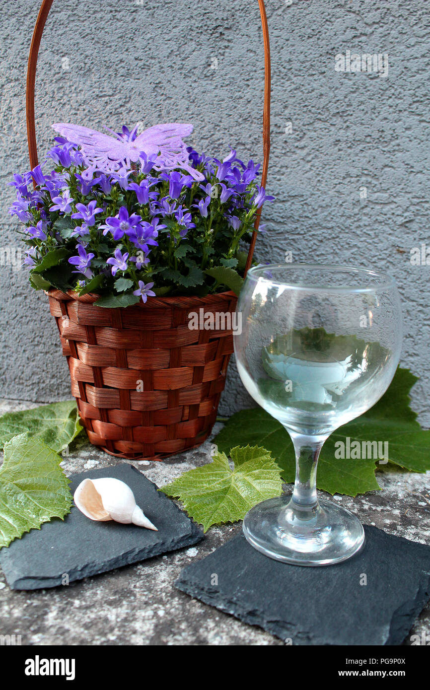 Still Life - uve blu con fiori viola in un cestello, foglie verdi e vuoto bicchiere da vino Foto Stock