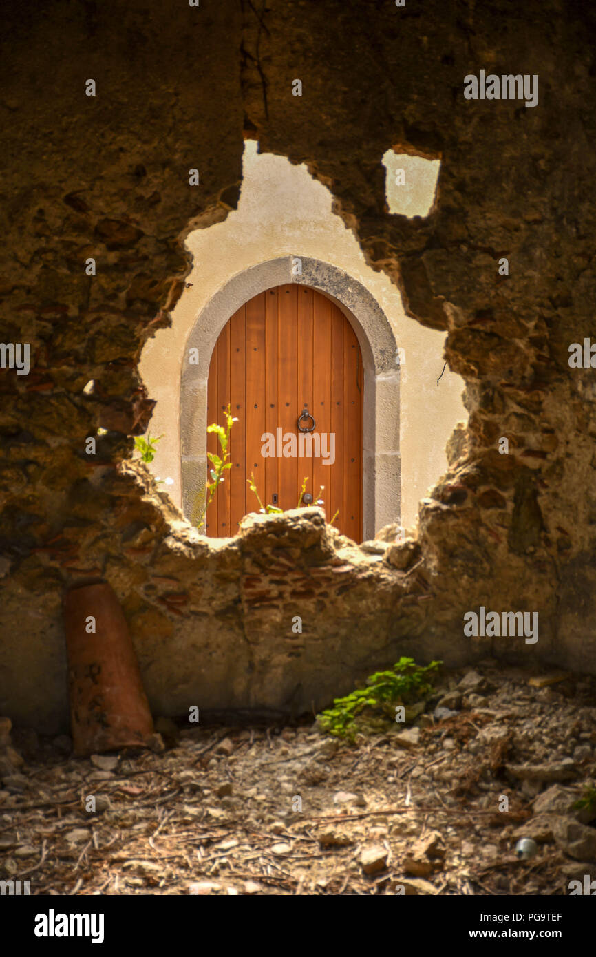 Un vecchio di legno porta ad arco in Sicilia visto attraverso la rottura di un foro in un muro di pietra Foto Stock