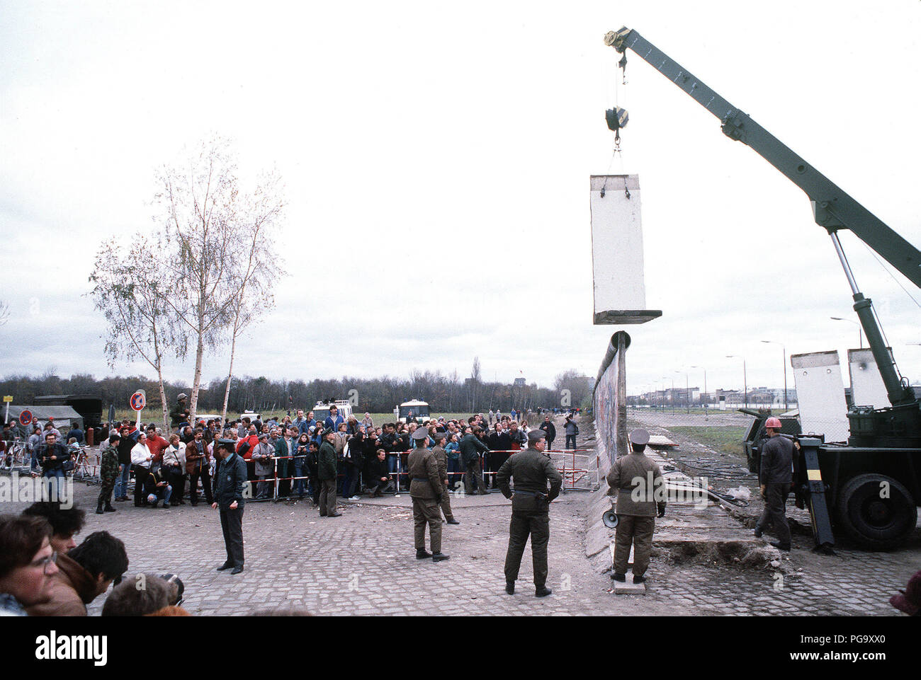 Muro di Berlino 1989 - Est della polizia tedesca e a ovest di cittadini tedeschi guardare come un operaio smantella una sezione del muro di Berlino a Potsdamer Platz. Foto Stock