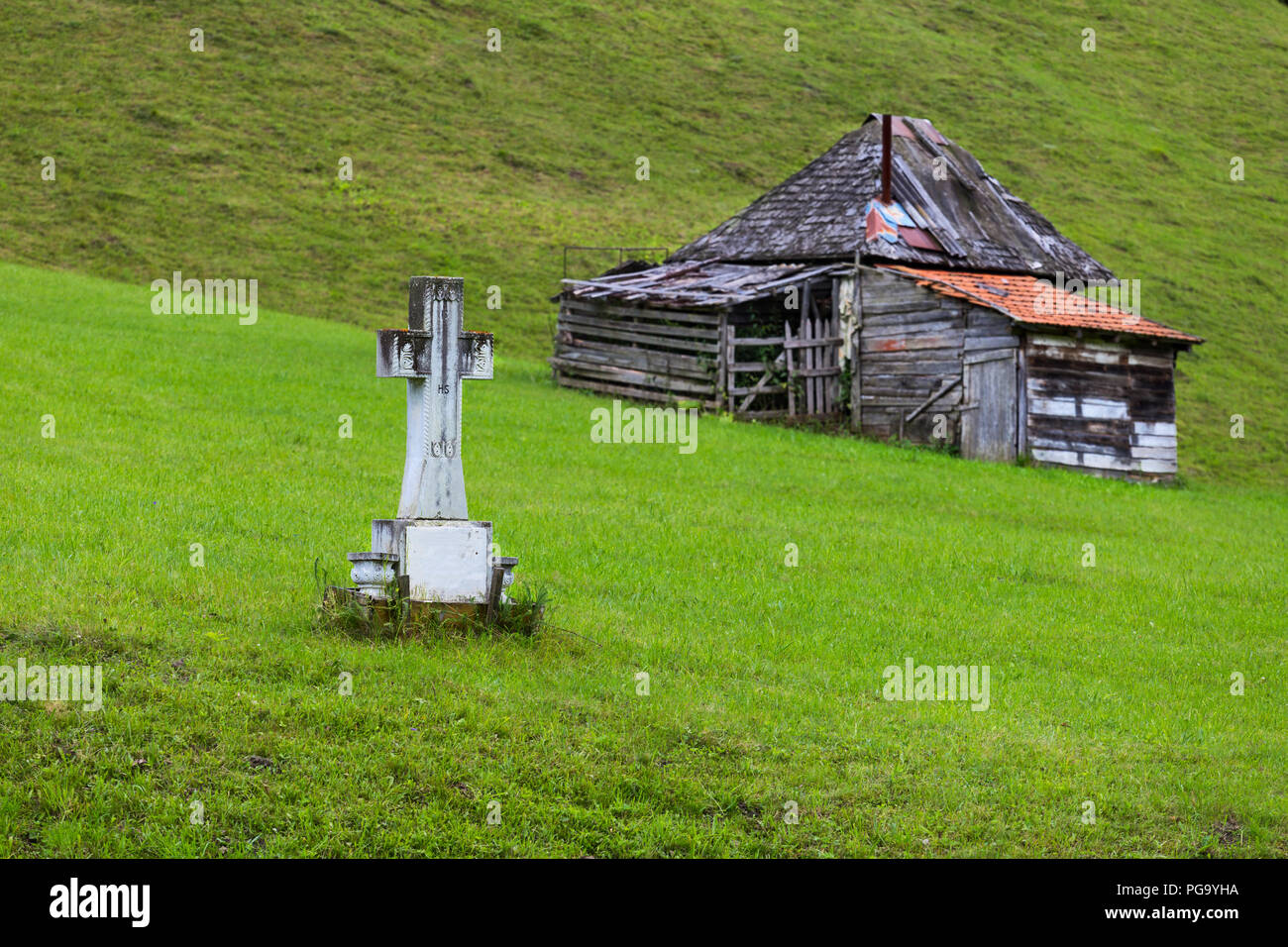 Croce di marmo vicino al modesto vecchia casa rumena, nella memoria degli anziani, in Romania zona di montagna Foto Stock