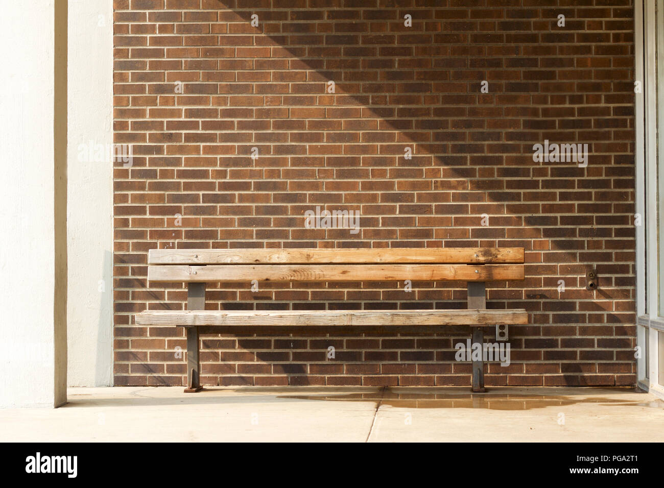 Vecchia panca in legno nella parte anteriore di un marrone weathered muro di mattoni sfondo con qualche ombra parziale nell'angolo superiore destro Foto Stock