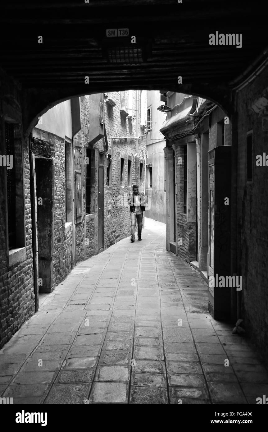 Venezia, Italia - 22 settembre 2016: uomo a camminare verso il basso una stretta viuzza centro di Venezia, Italia, monocromatico Foto Stock