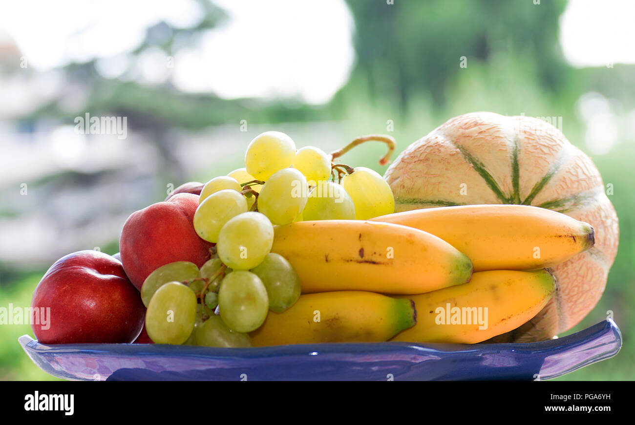 Set di frutta, melone, banane, uva e pesche, su un vassoio con sfondo verde Foto Stock