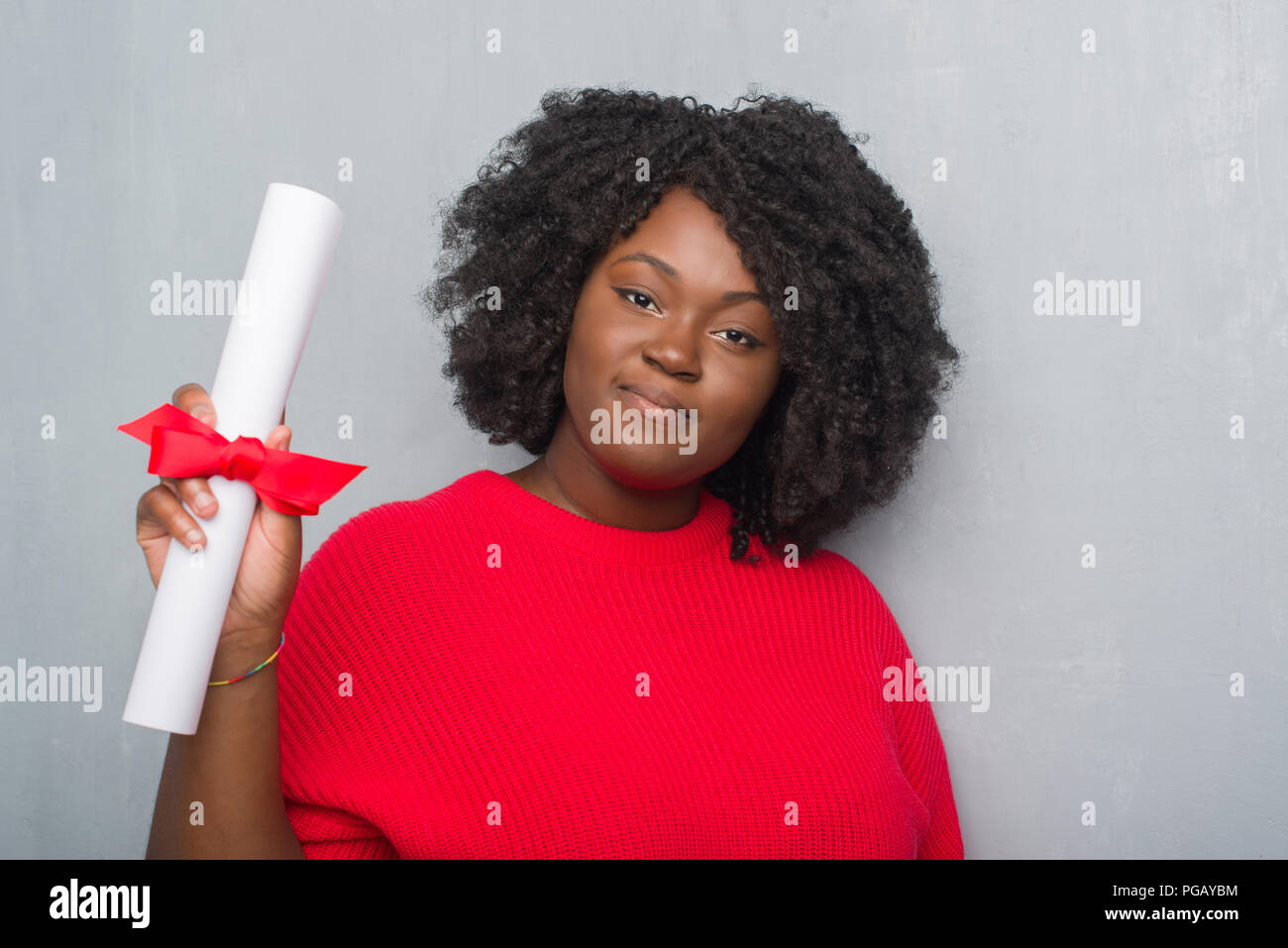 Giovane africano donna americana su grigio parete grunge holding diploma con un fiducioso espressione sul viso intelligente pensare grave Foto Stock