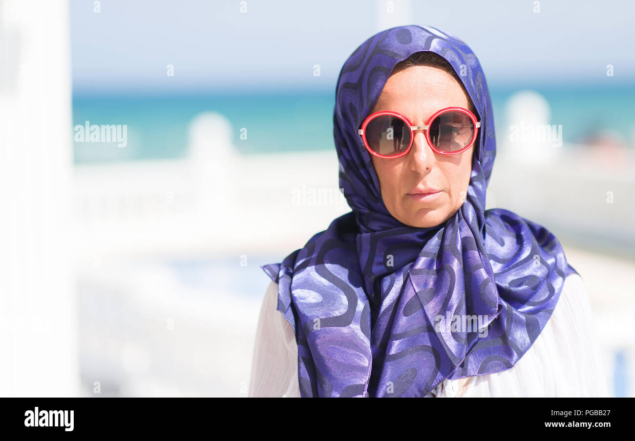 La mezza età brunette donna araba presso la piscina di indossare occhiali da sole con un fiducioso espressione sul viso intelligente pensare grave Foto Stock