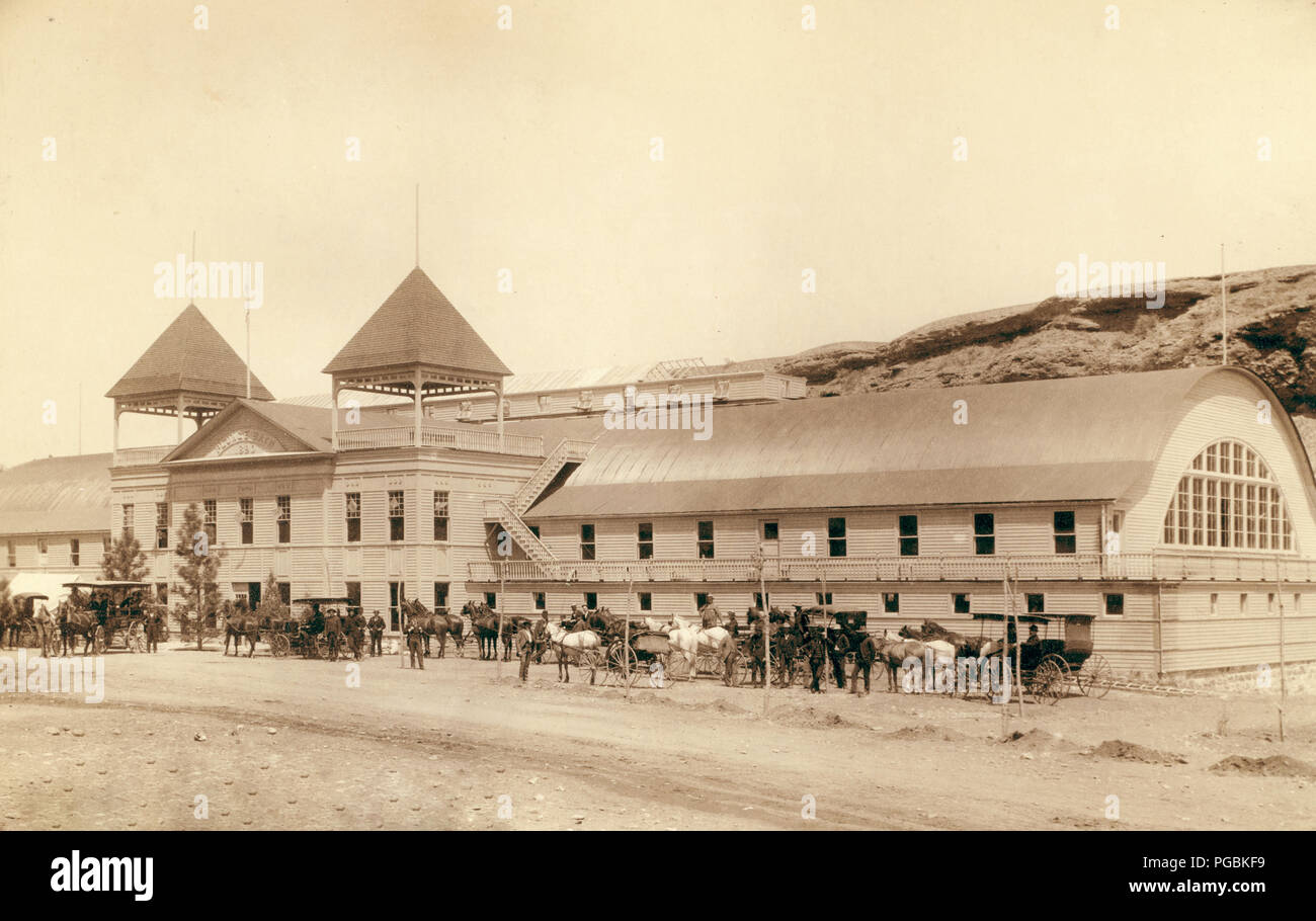 Grande edificio con alcuni cavalli e carrozze davanti. Foto Stock