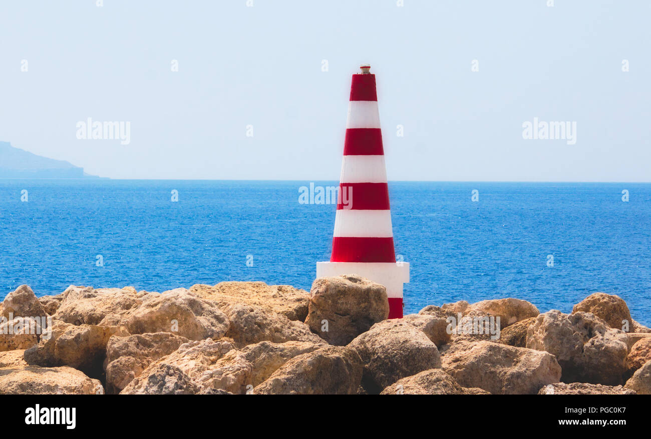 A strisce rosse e bianche mare faro di sicurezza fissati sulle rocce in porto con l'orizzonte di acqua in background in una limpida giornata di sole con un cielo blu Foto Stock
