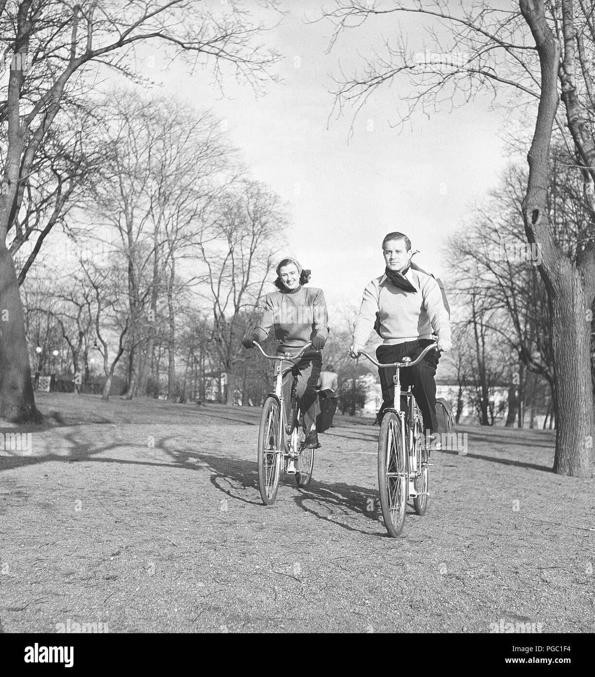 1940s giovane sulle biciclette. Una giovane coppia è cavalcare le loro biciclette su una soleggiata giornata di primavera. Essi hanno pratiche buste attaccata alla rastrelliera delle biciclette in cui essi potrebbero trasportare il picnic food. La Svezia 1947. Foto Kristoffersson AB11-11 Foto Stock