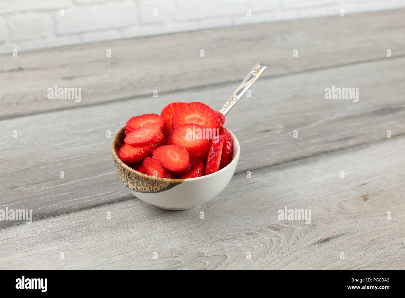 Piccolo recipiente pieno di pezzi di fragola, cucchiaio - snack sani pronto a mangiare. Foto Stock