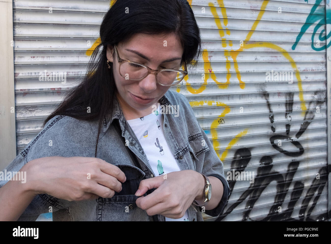 Giovane donna adulta che indossano occhiali aprendo una maglietta poket sulla strada, Foto Stock