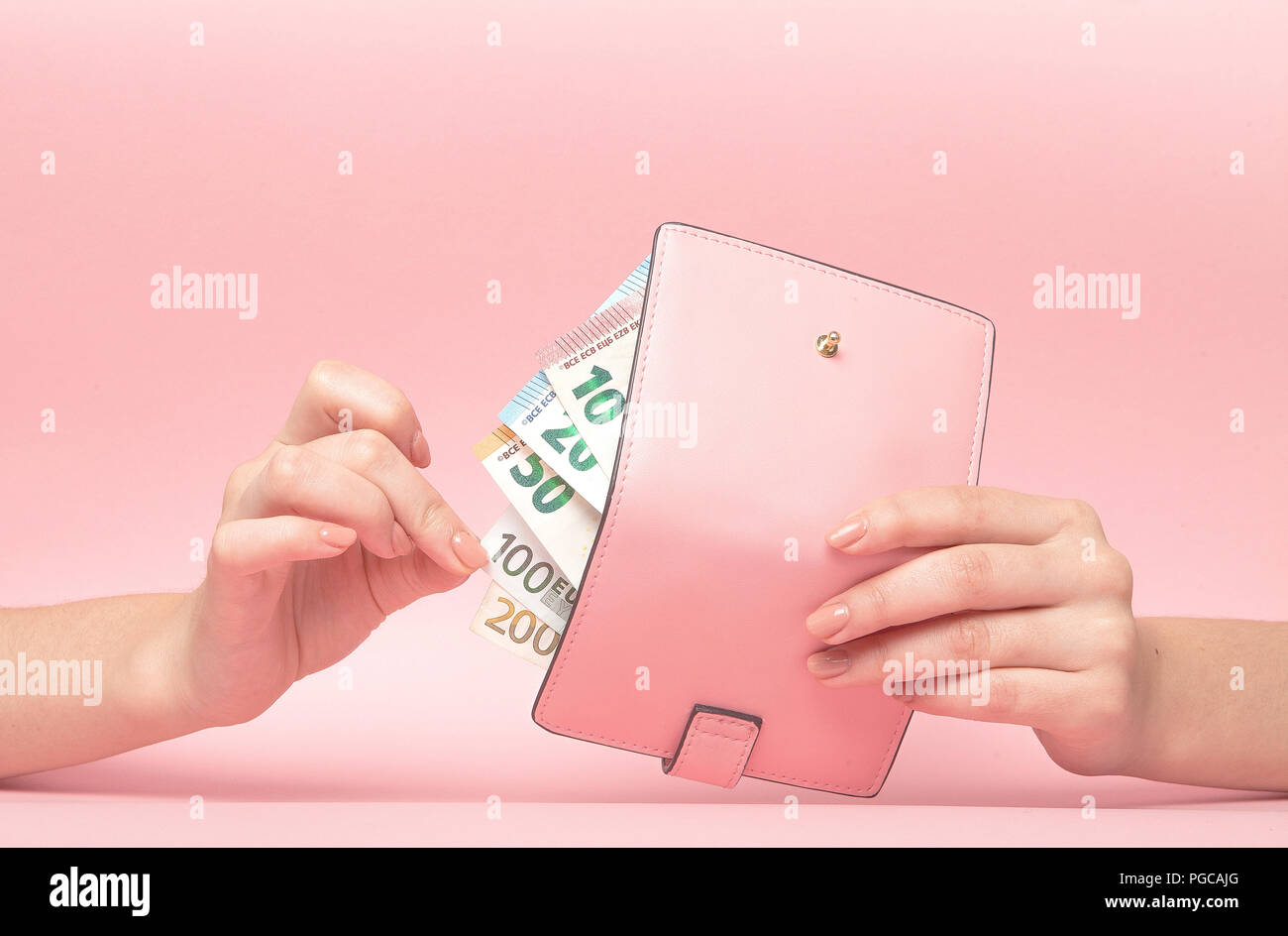 Borsa rosa e le banconote in euro in mani femminili su sfondo rosa. Il concetto di business. Foto Stock