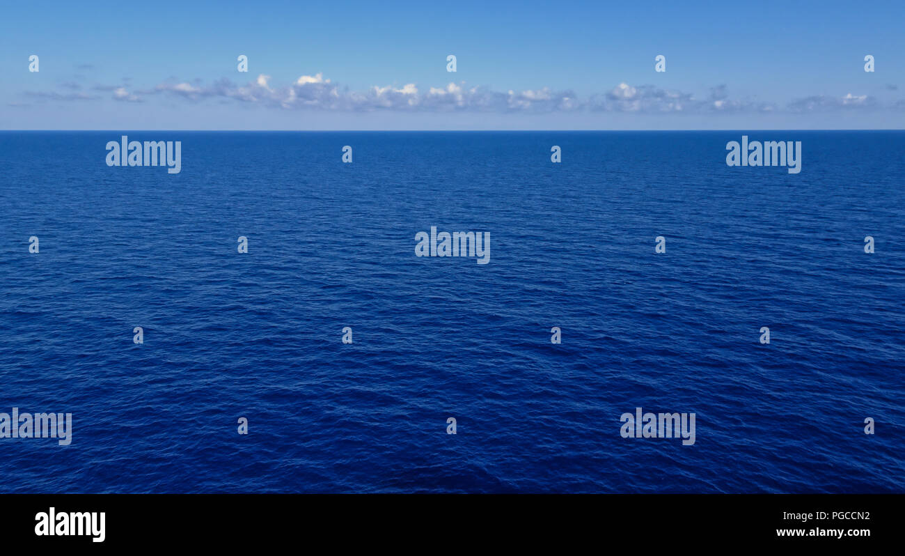 Molto calma blu scuro oceano con alcune nuvole e la luce blu del cielo all'orizzonte Foto Stock