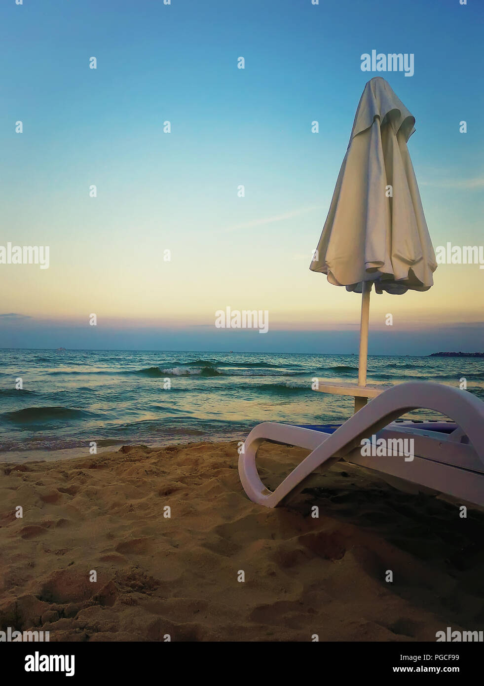 Bella vista al tramonto come una sedia a sdraio con ombrellone sulla spiaggia di sabbia di fronte a un mare blu dell'acqua. Foto Stock