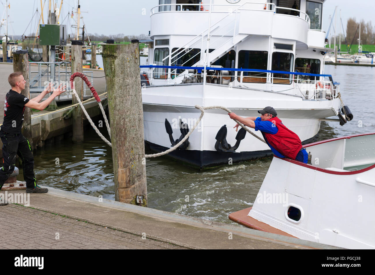 Due piccoli battellieri gettare una fune alla manovra di docking dell'arrivo di una nave passeggeri nel porto di Carolinensiel. Foto Stock