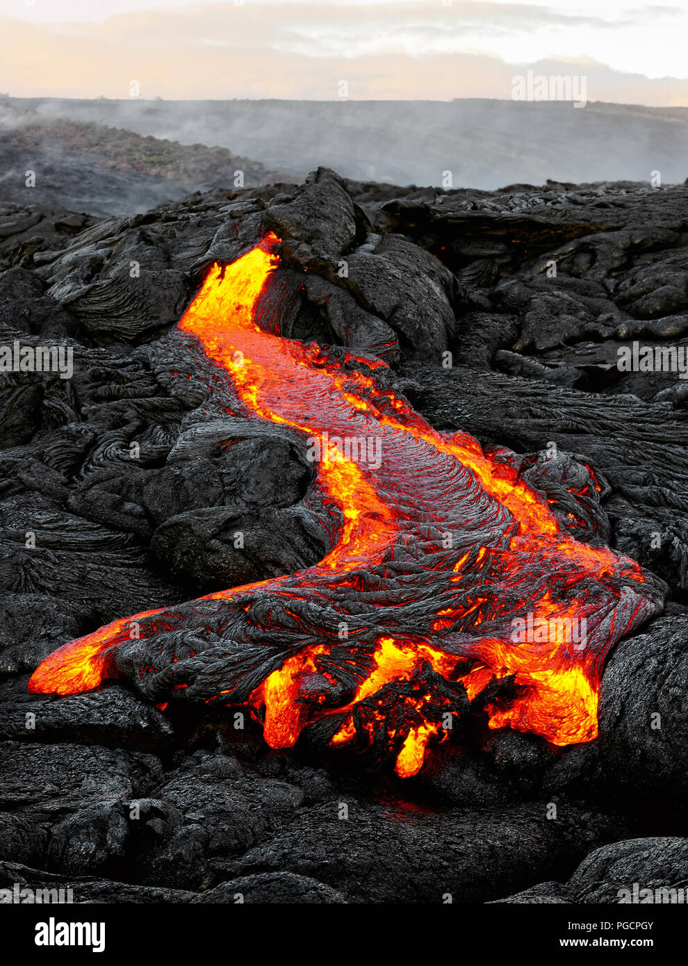 Un flusso di lava emerge da una colonna di terra e scorre in un nero paesaggio vulcanico, nel cielo mostra la prima luce del giorno - Ubicazione: Hawaii, Big Island, Foto Stock