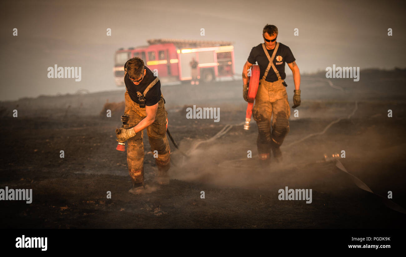 I Vigili del fuoco trascinare tubi flessibili e discutere i piani durante la Saddleworth Moor incendi Foto Stock