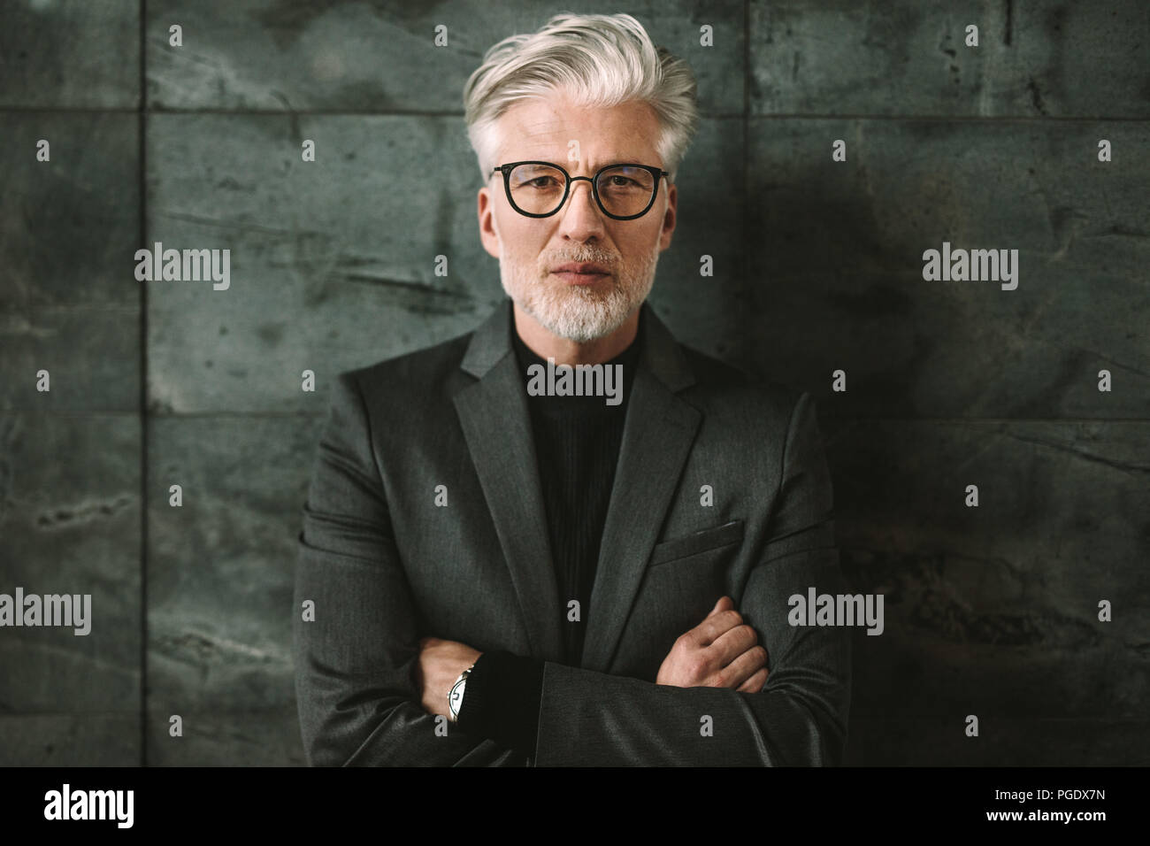 Ritratto di fiducioso imprenditore maturo in piedi contro uno sfondo grigio. Bel maschio in bicchieri in piedi con le braccia incrociate e guardando a ca Foto Stock