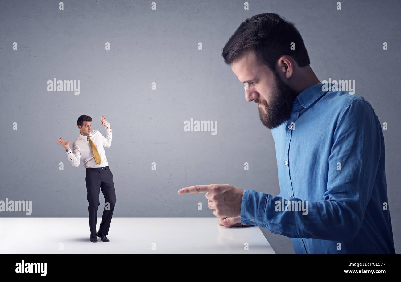 Giovane imprenditore professionale essendo arrabbiato con un altro imprenditore in miniatura di fronte a uno sfondo grigio Foto Stock