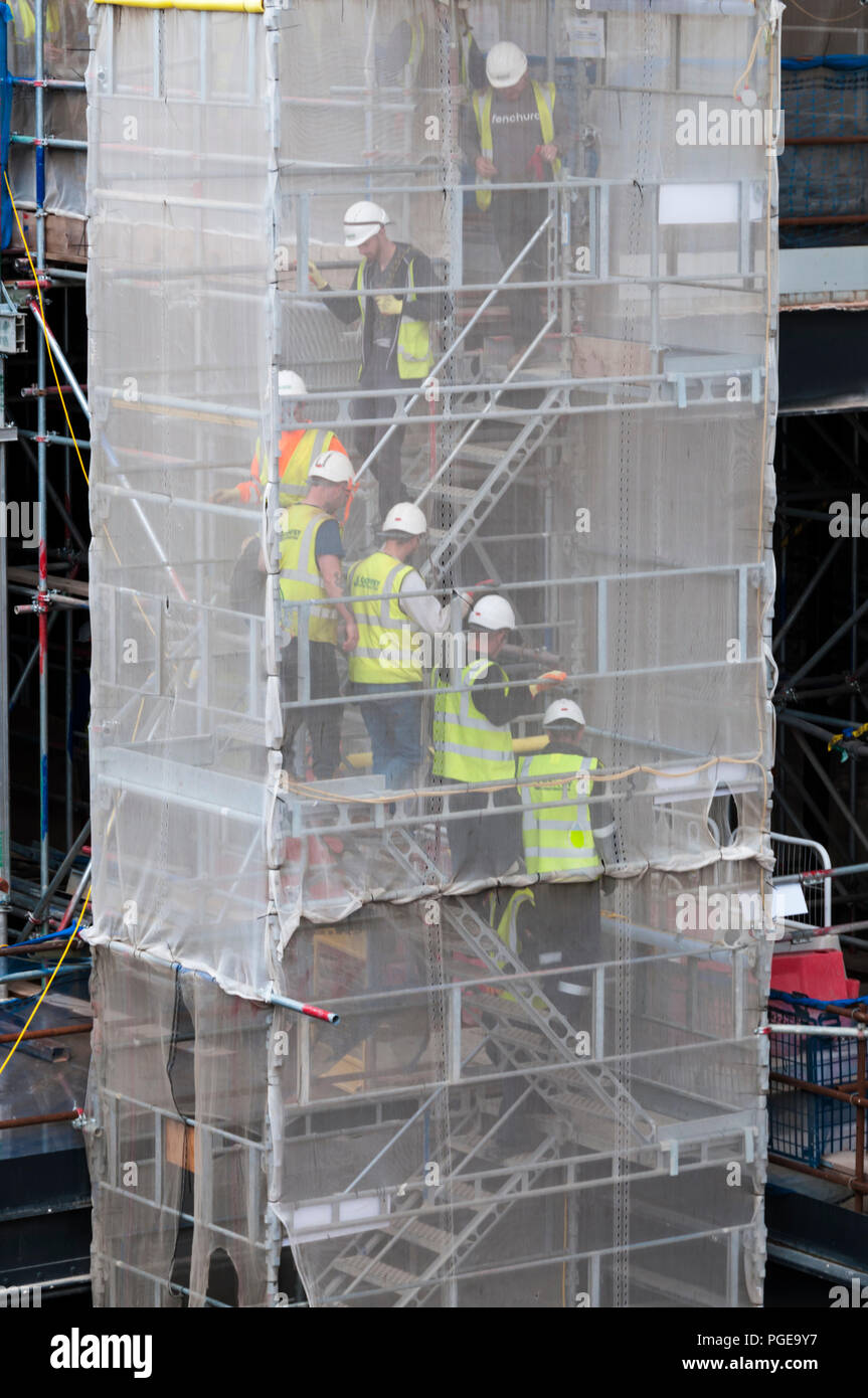 Lavoratori edili scendendo una scala temporanea impalcatura dietro di pacciamatura. Foto Stock