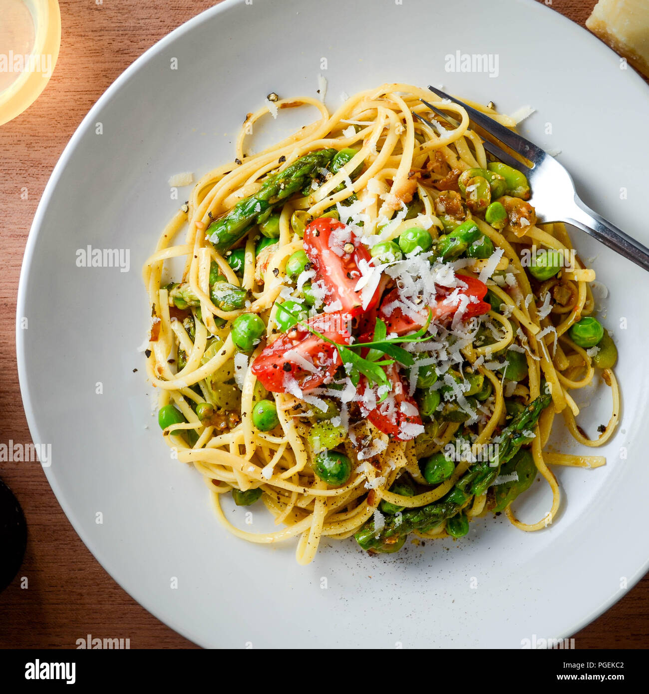 Pasta primavera con fave, piselli sgranati, asparagi e pomodori ciliegini, guarnita con formaggio Reggiano-Parmigiano, raffigurate piatte-lay. Foto Stock