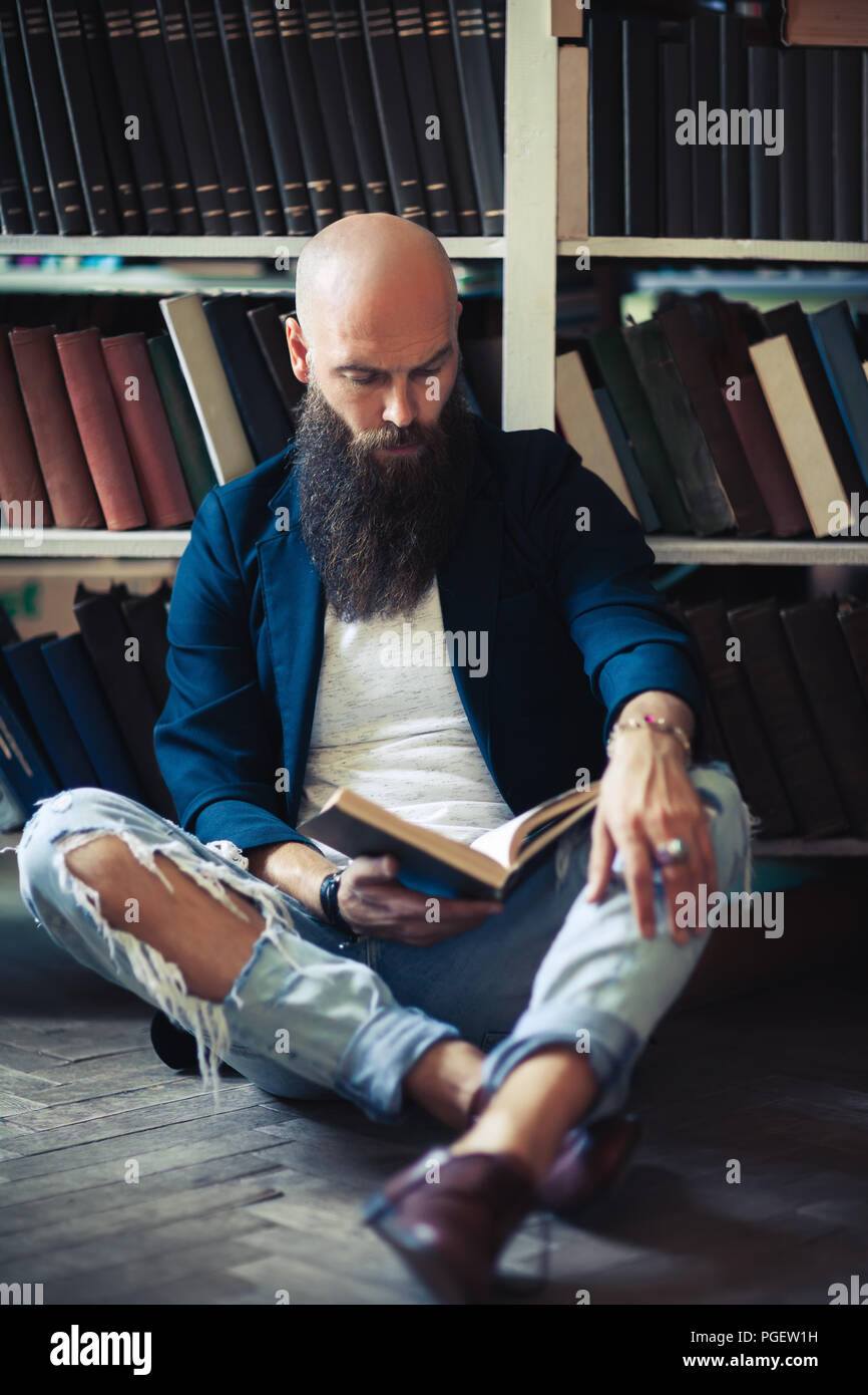 Bello barbuto uomo seduto sul pavimento, la lettura di libri e rilassante in biblioteca o in libreria Foto Stock