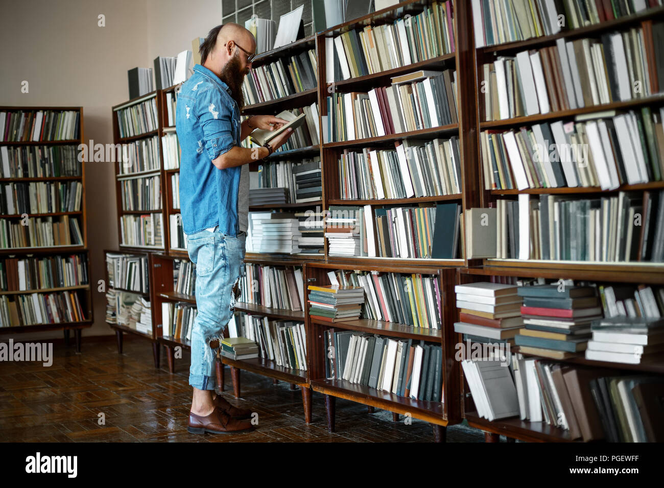 A piena lunghezza Ritratto di elegante uomo barbuto libro di lettura nella libreria o nella libreria. Il concetto di istruzione Foto Stock